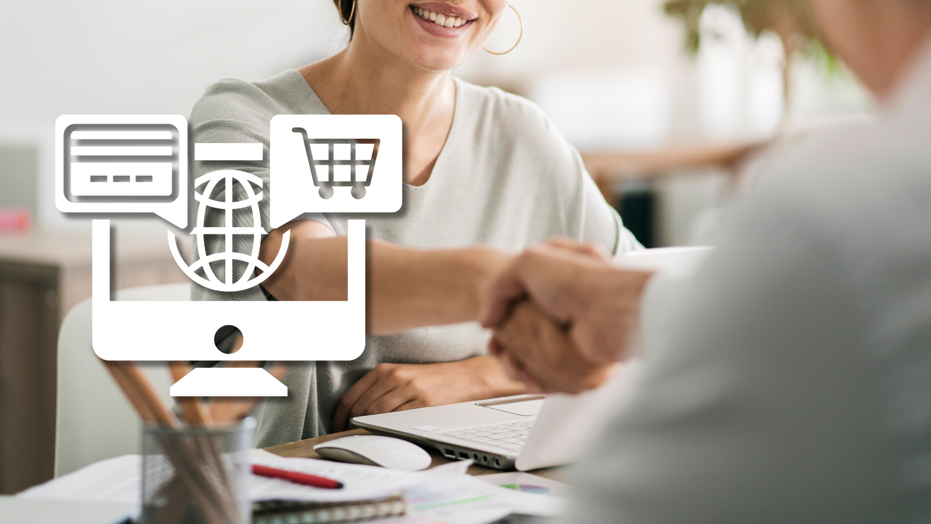 Uścisk dłoni przy biurku z laptopem, obok biała ikona sklepu internetowego – zatrudnienie specjalisty e-commerce na etat